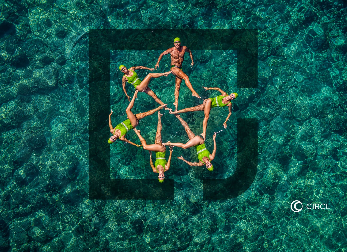 Seven swimmers in green forming a circle on open water, shot from above